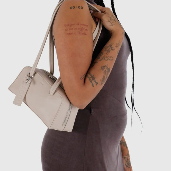 Person holding a beige handbag against a plain background