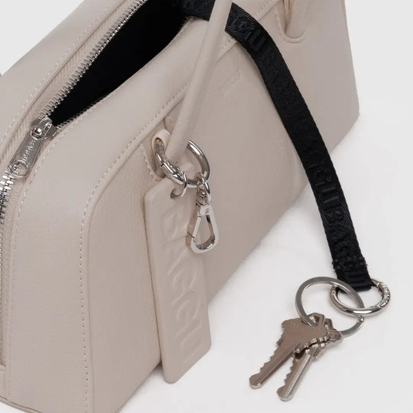 Beige handbag with a black strap and keychain on a white background