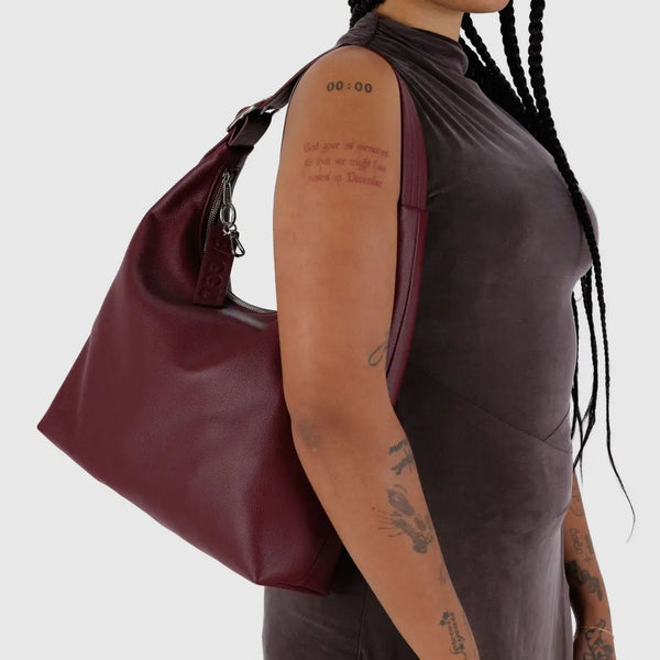 Person holding a maroon handbag against a white background