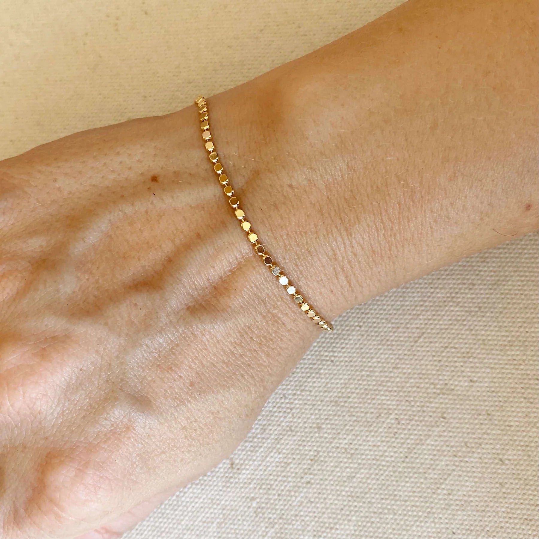 Gold bracelet on a wrist against a neutral background