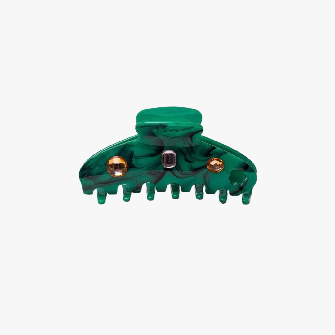 A green tortoiseshell hair claw clip with gold-tone metal accents and a small central rhinestone, shown on a light gray background.