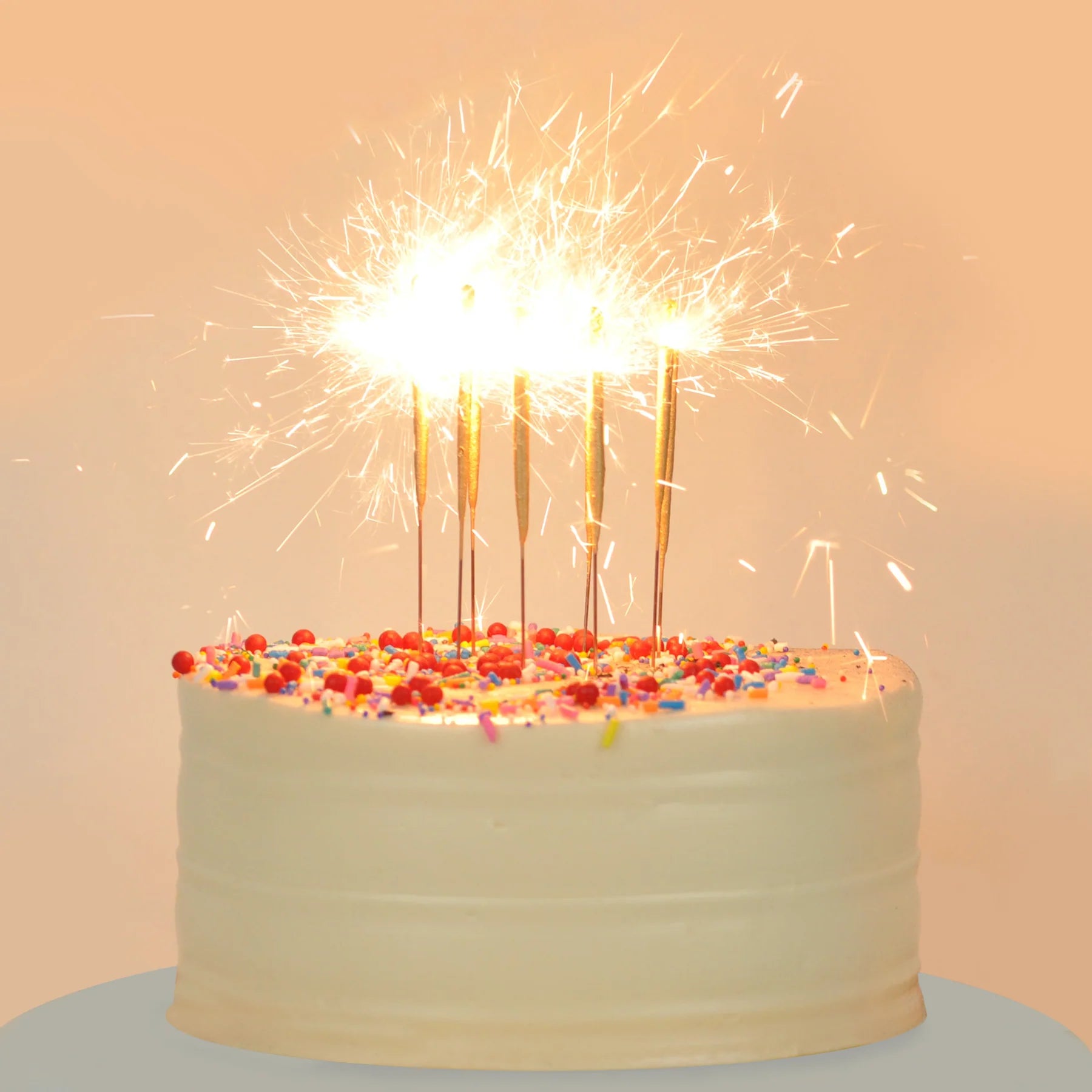 Birthday cake with lit sparklers on a light background