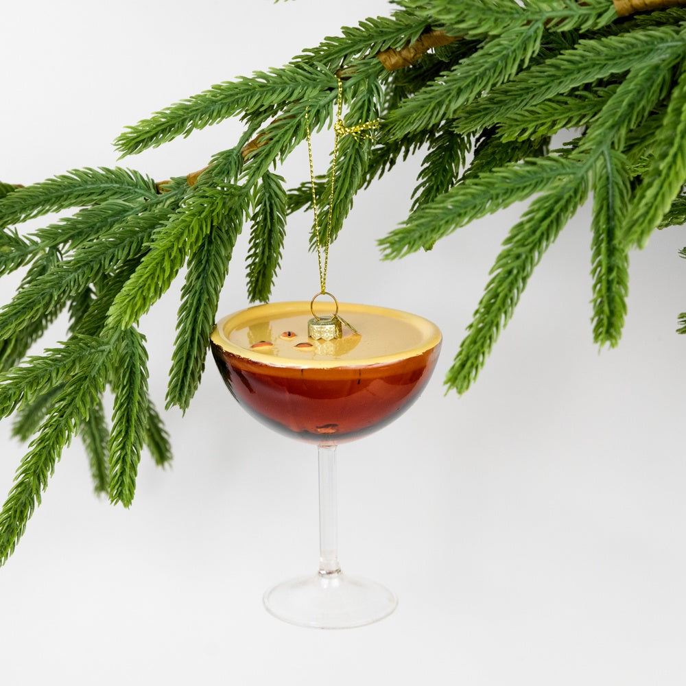 Decorative ornament shaped like a cocktail glass with a brown drink, hanging from a Christmas tree branch.