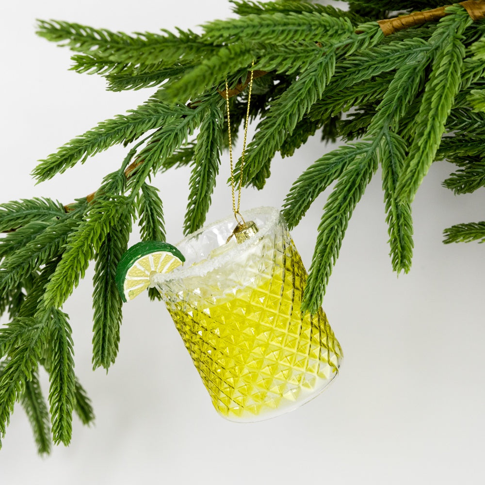 Decorative glass ornament shaped like a teapot with lime garnish hanging from a Christmas tree.
