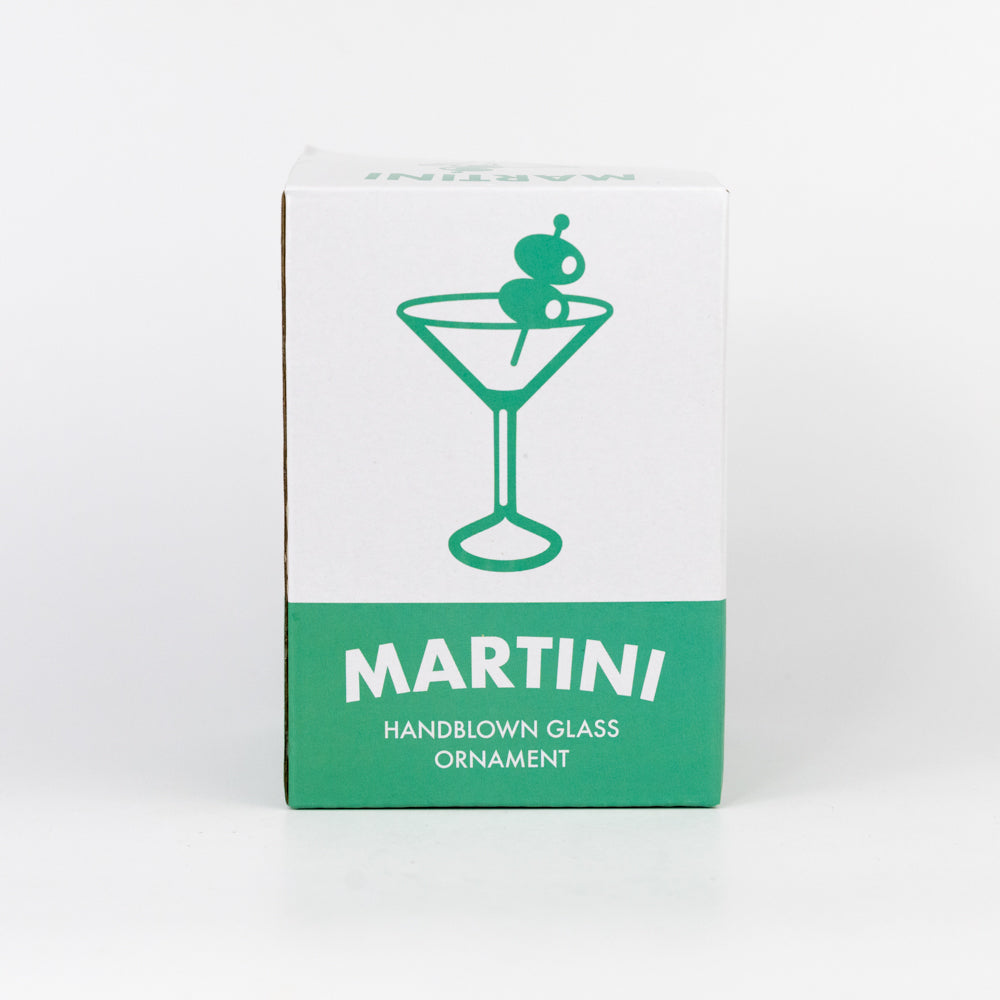 Decorative martini ornament with two olives on a toothpick hanging from a branch against a white background.