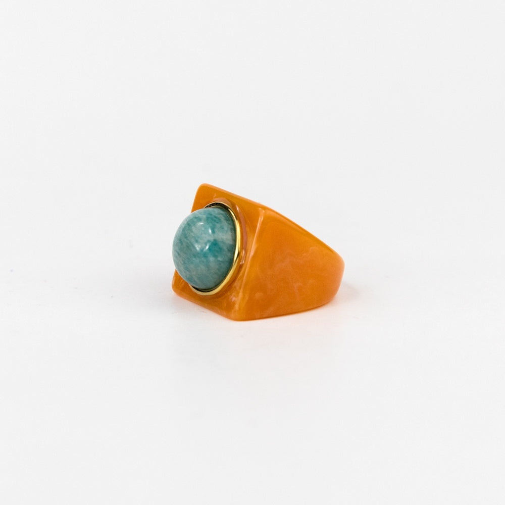 Ring with a turquoise gemstone in an orange setting on a white background