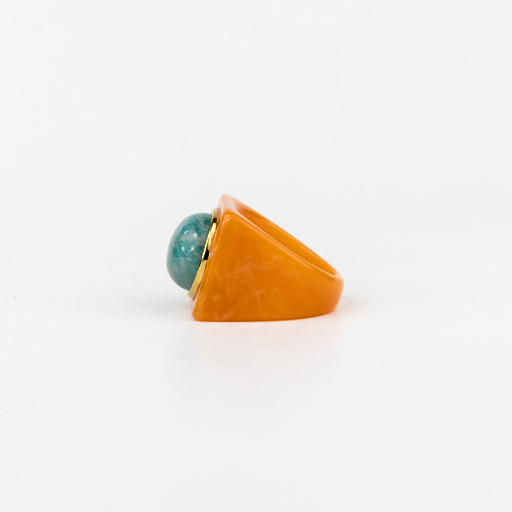 Ring with a turquoise bead and orange triangular stone on a white background