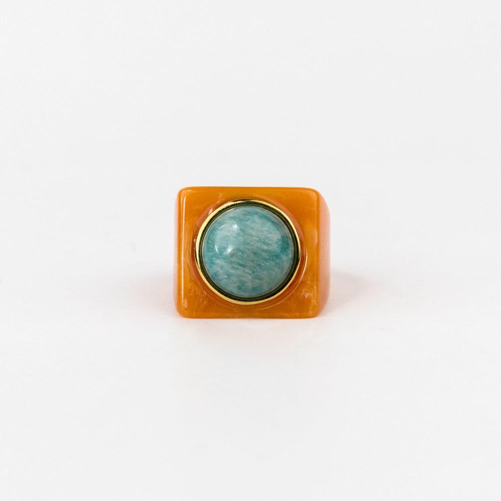 Ring with a square orange band and central green gemstone on a white background