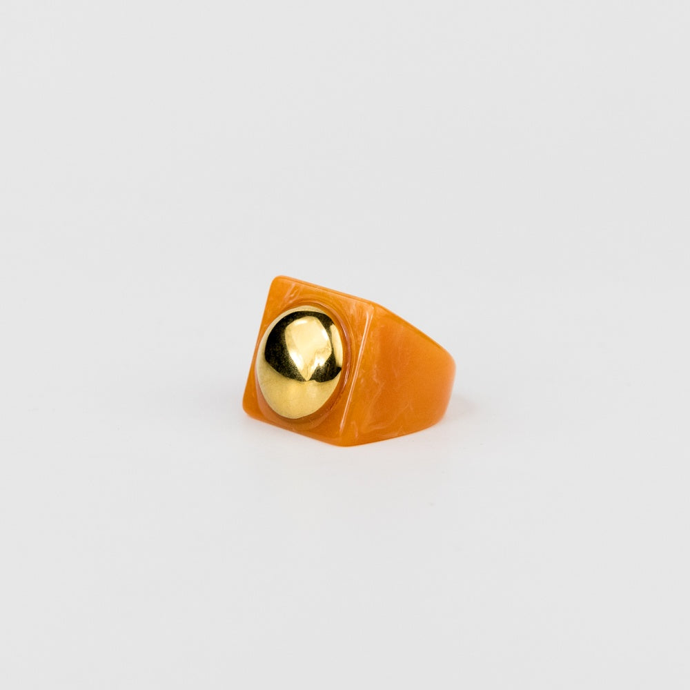 Orange ring with a gold ball on a light gray background