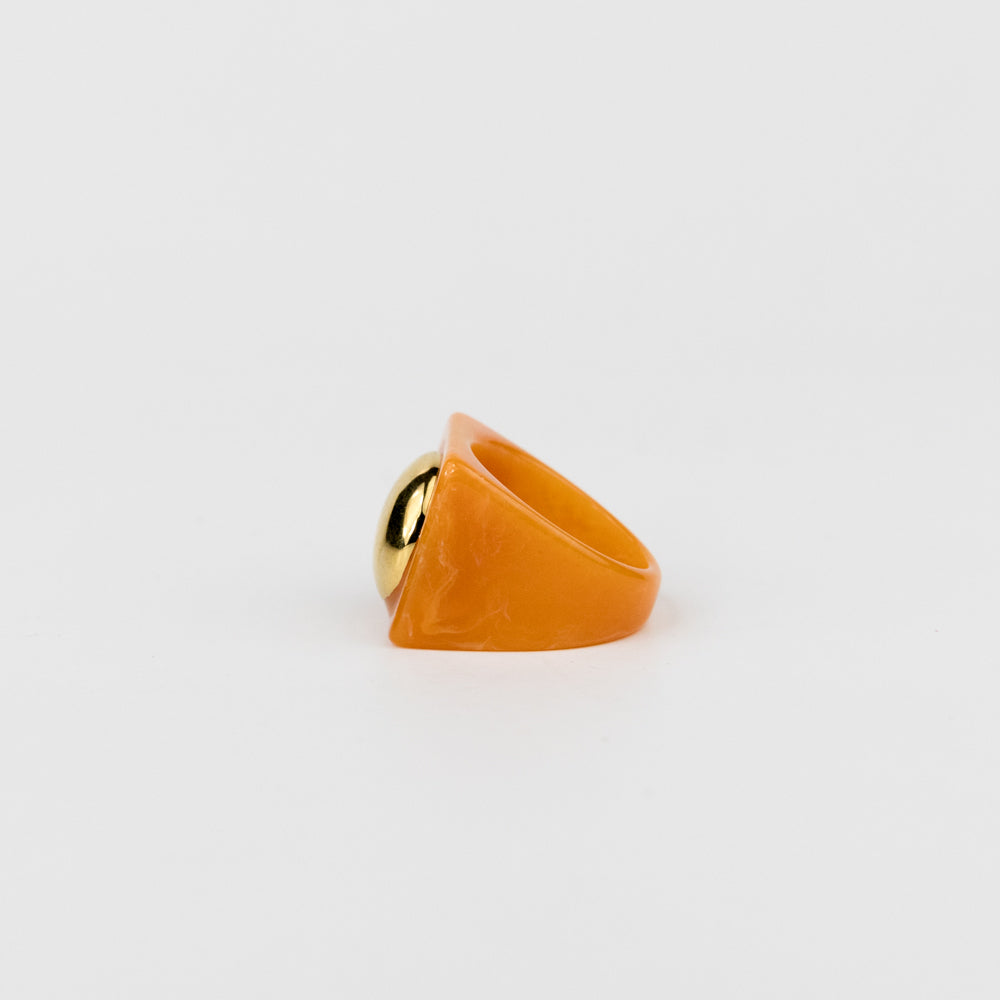Gold ring with a large orange stone on a light gray background