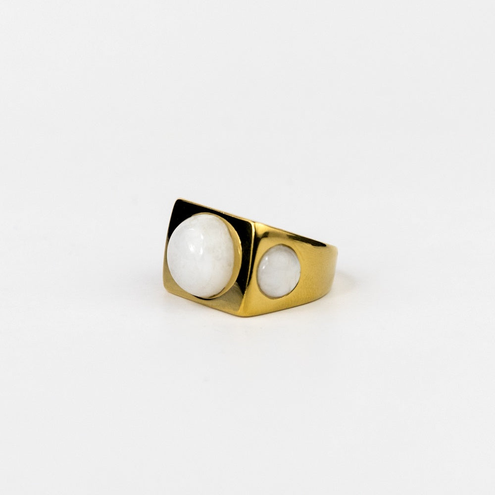 Gold ring with two white stones on a light gray background