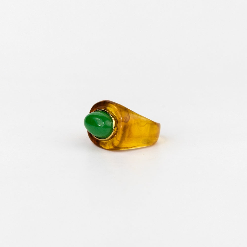 Ring with a green gemstone and amber-colored band on a white background