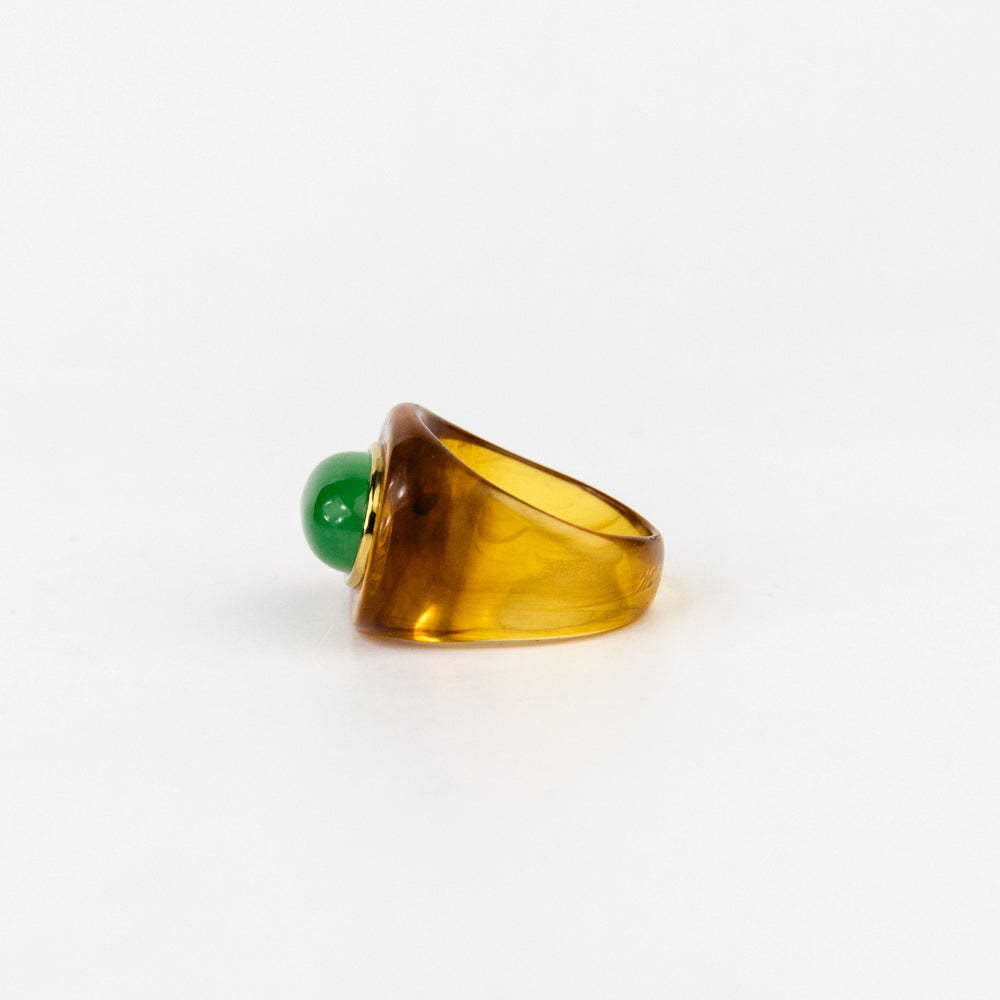 Ring with a green bead and amber-colored band on a white background