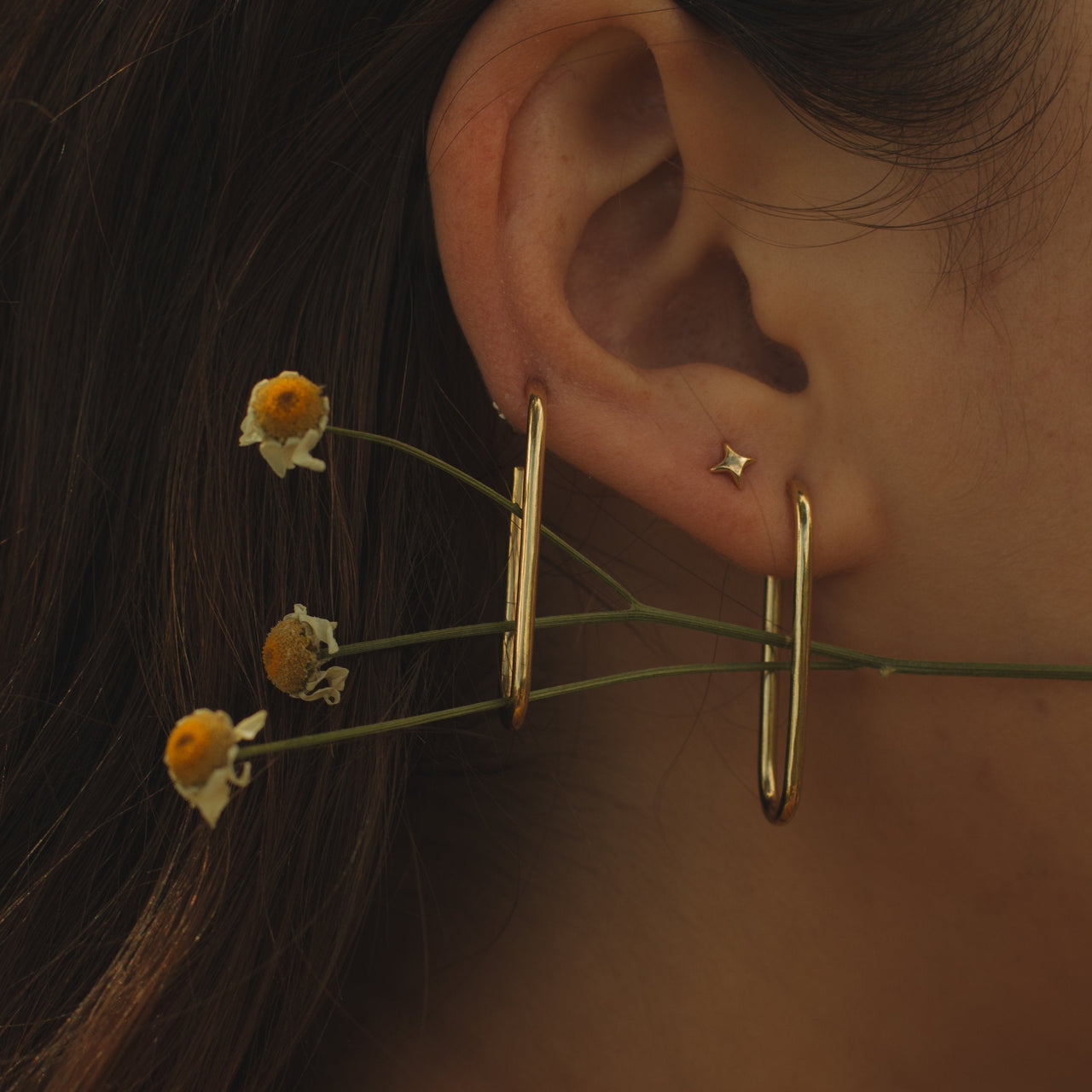 Elongated gold hoop earrings on a light gray background