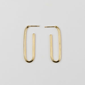 Elongated gold hoop earrings on a light gray background