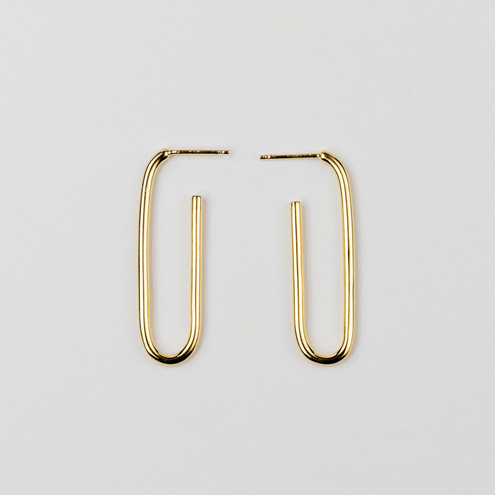 Elongated gold hoop earrings on a light gray background