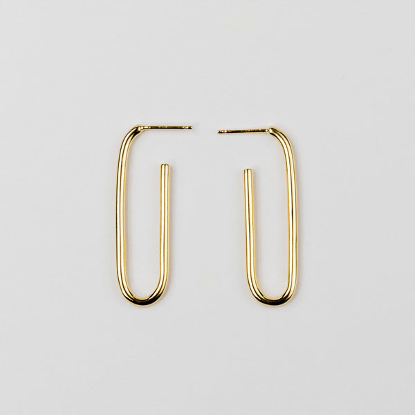 Elongated gold hoop earrings on a light gray background
