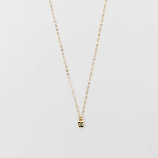 Gold necklace with an opal gemstone pendant on a light gray background