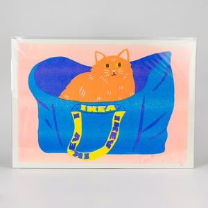 Print of a cat in a blue IKEA bag branding on a pink background