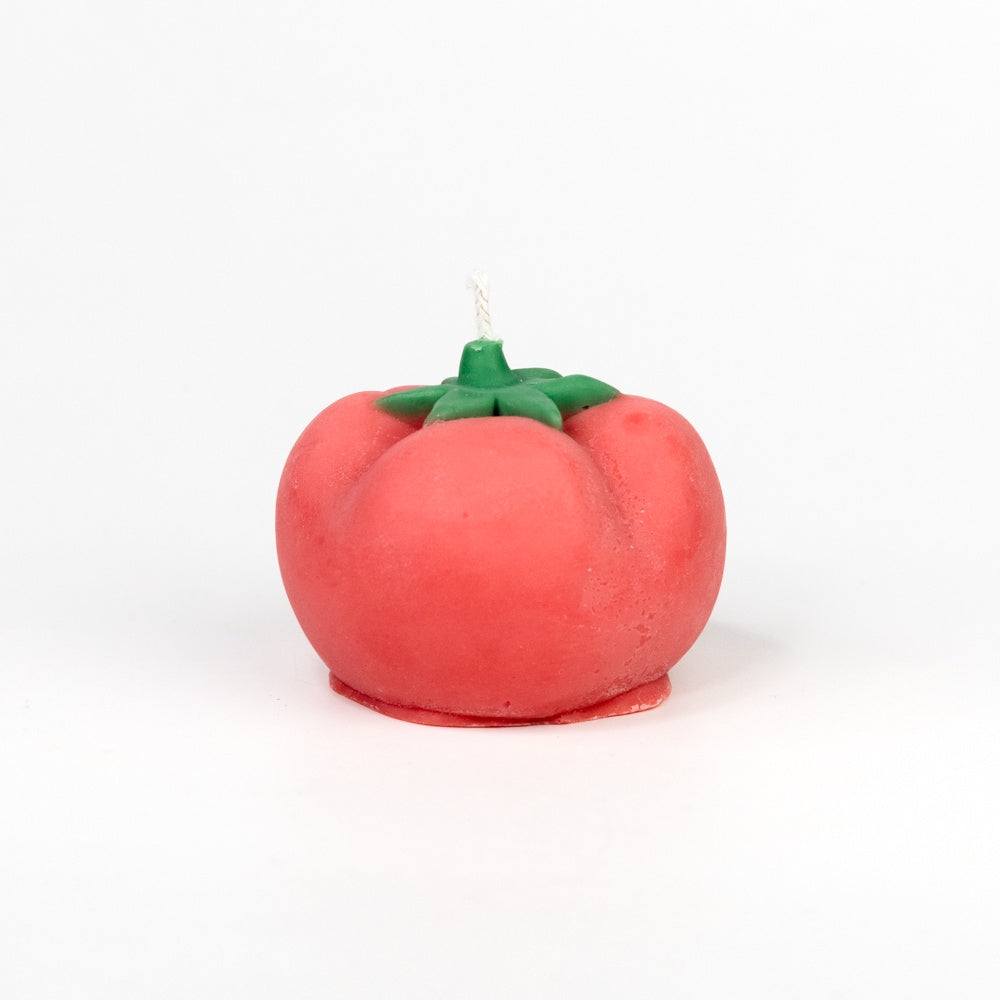 Tomato-shaped candle with green stem on a white background