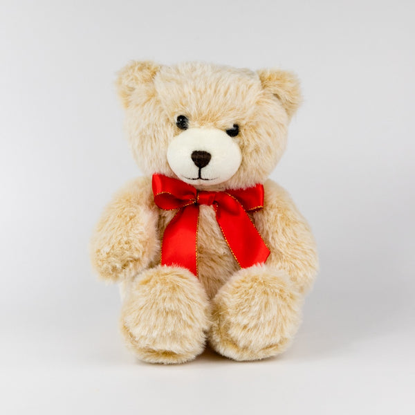 Beige teddy bear with a red bow on a white background
