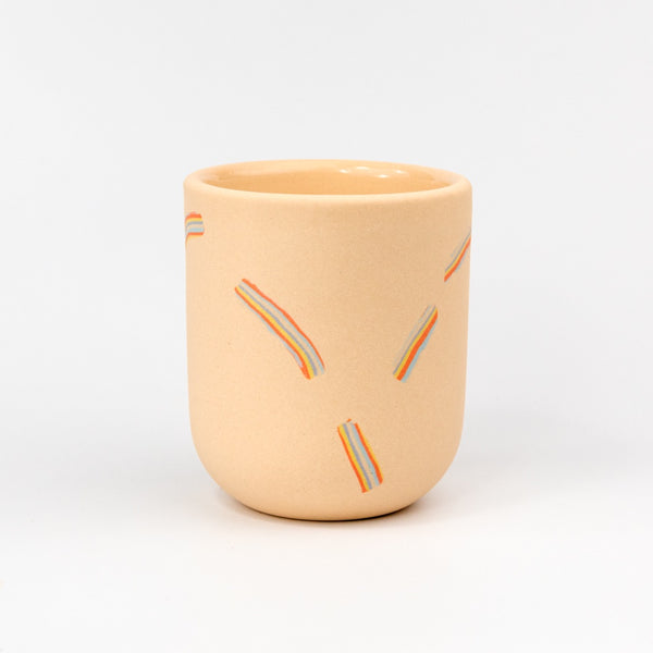 Light pink ceramic cup with decorative rainbow lines on a white background