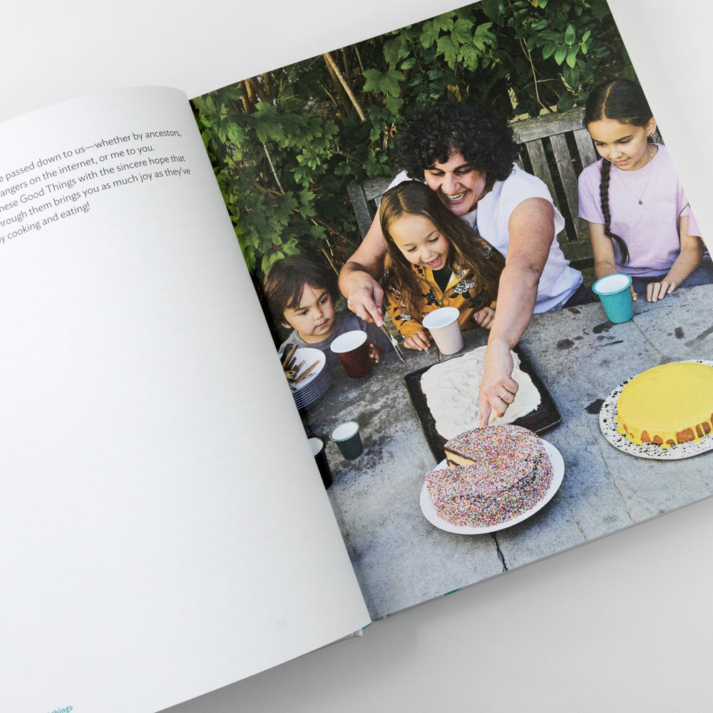 Open book showing a family baking outdoors with a cake on a table.
