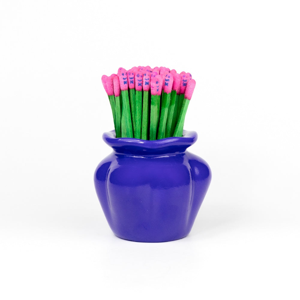 Blue vase with matchsticks with green stems and pink tops resembling a flower bouquet on a white background