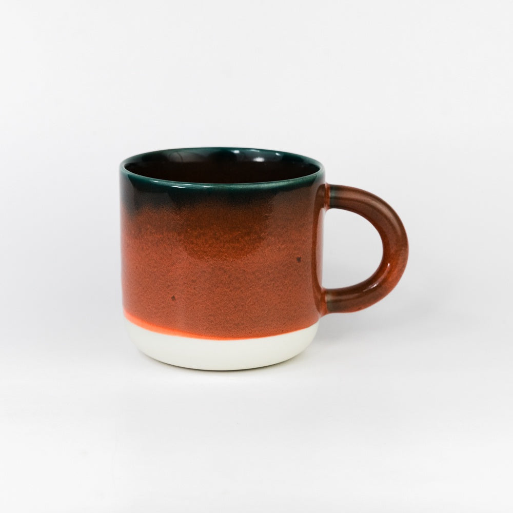 Ceramic mug with gradient color from green to brown on a white background