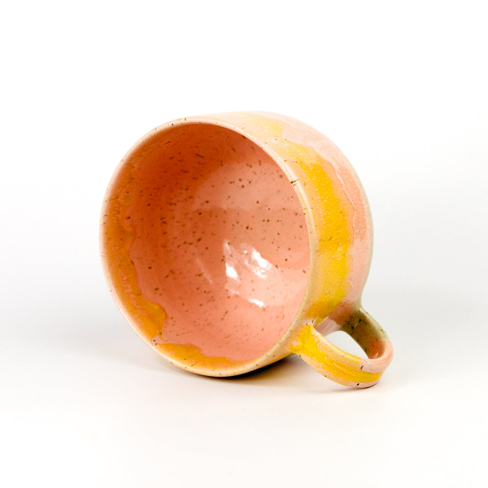 Ceramic mug with speckled orange interior and yellow exterior on a white background