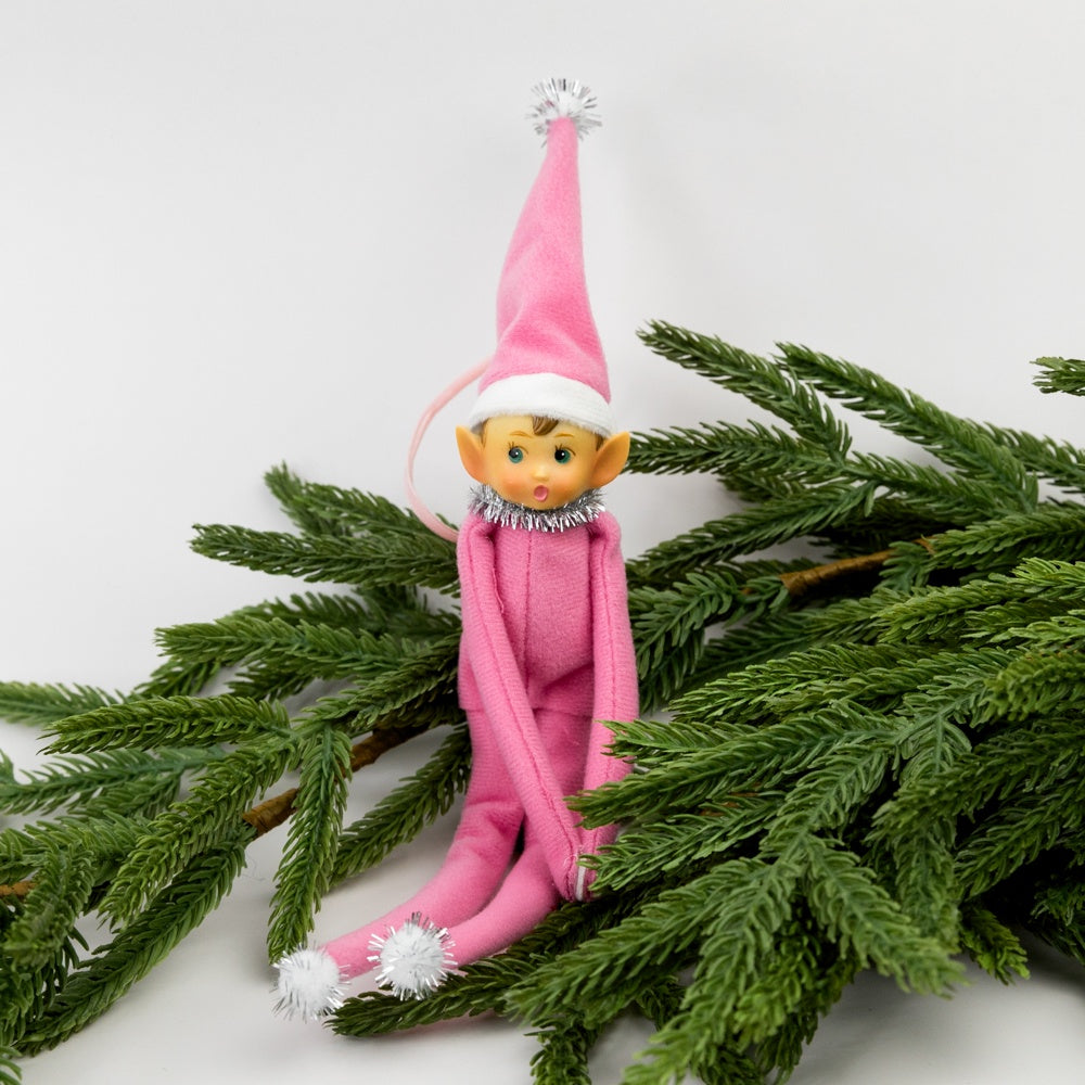 Pink elf doll sitting on green branches against a white background