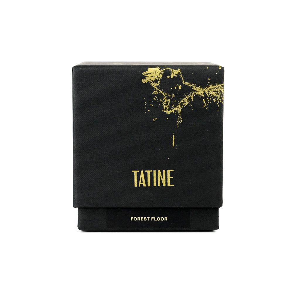 A clear glass candle with a green wax layer and the brand name 'tatine' visible on the side.