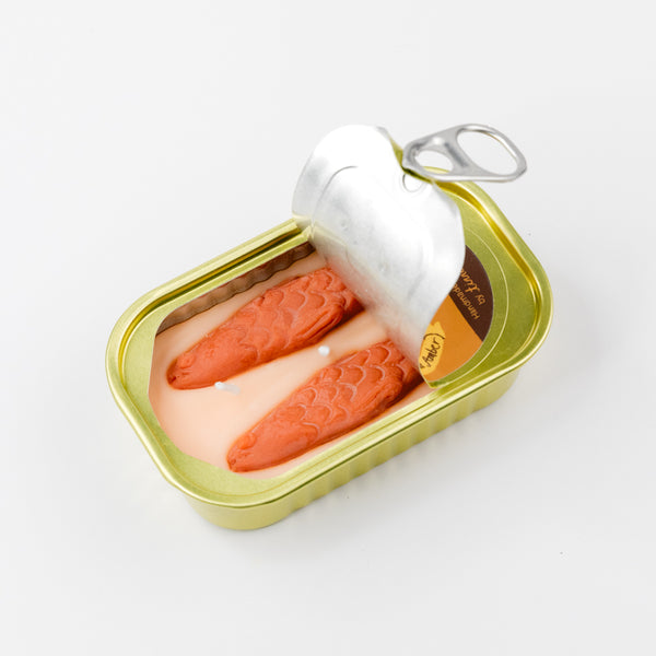 tinned candle designed to look like a  sardine can with the top peeled back to expose sardine shapes in the wax on a white background