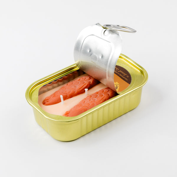tinned candle designed to look like a  Sardine can with the top peeled back to expose sardine shapes in the wax on a white background