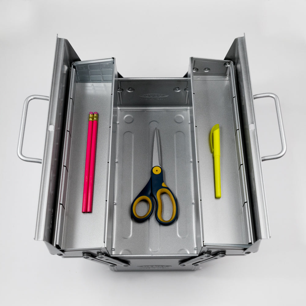 Metal drawer with stationery items including pink pencils, scissors, and a yellow pen on a white background.