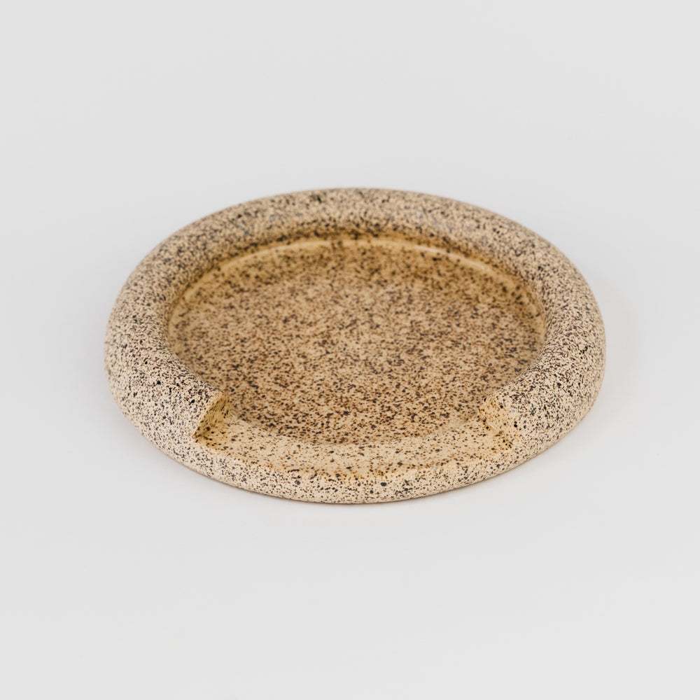 Round ceramic plate with speckled texture on a light gray background