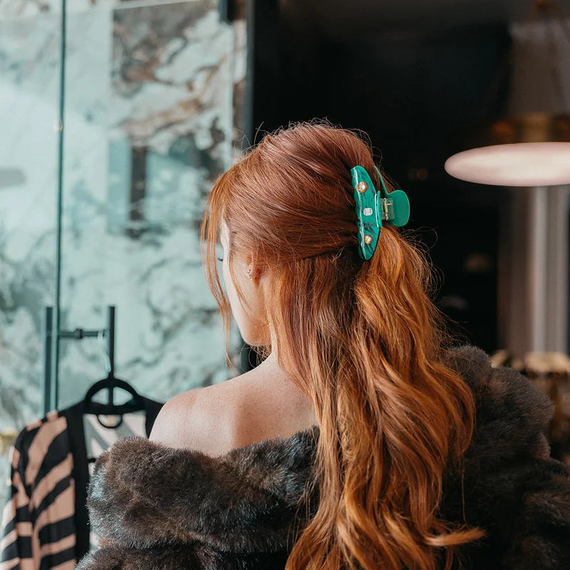A green tortoiseshell hair claw clip with gold-tone metal accents and a small central rhinestone, shown on a light gray background.