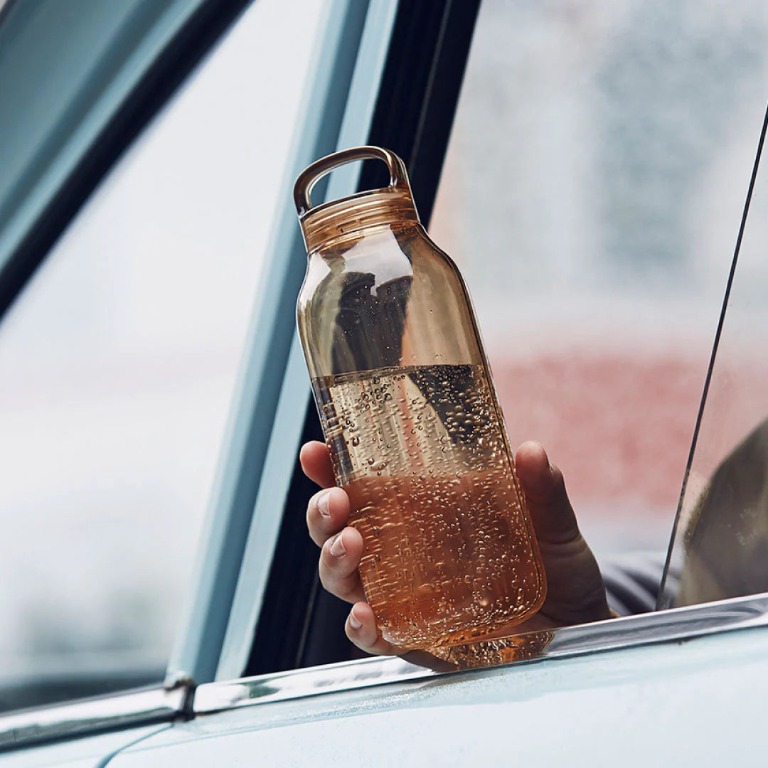 Hand holding a transparent water bottle with a car window in the background