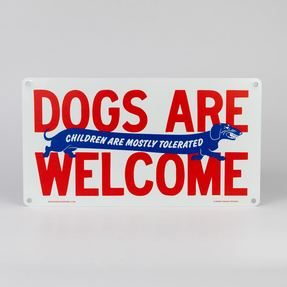 Metal sign with red text 'DOGS ARE WELCOME' and blue text 'CHILDREN ARE MOSTLY TOLERATED' on a white background.