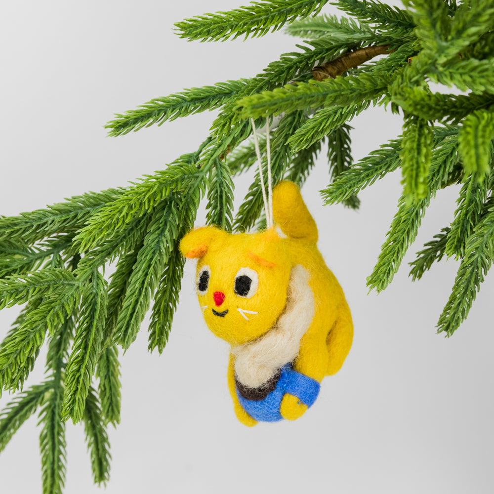 Yellow felted cat ornament holding a steaming cup of cocoa hanging from a tree branch
