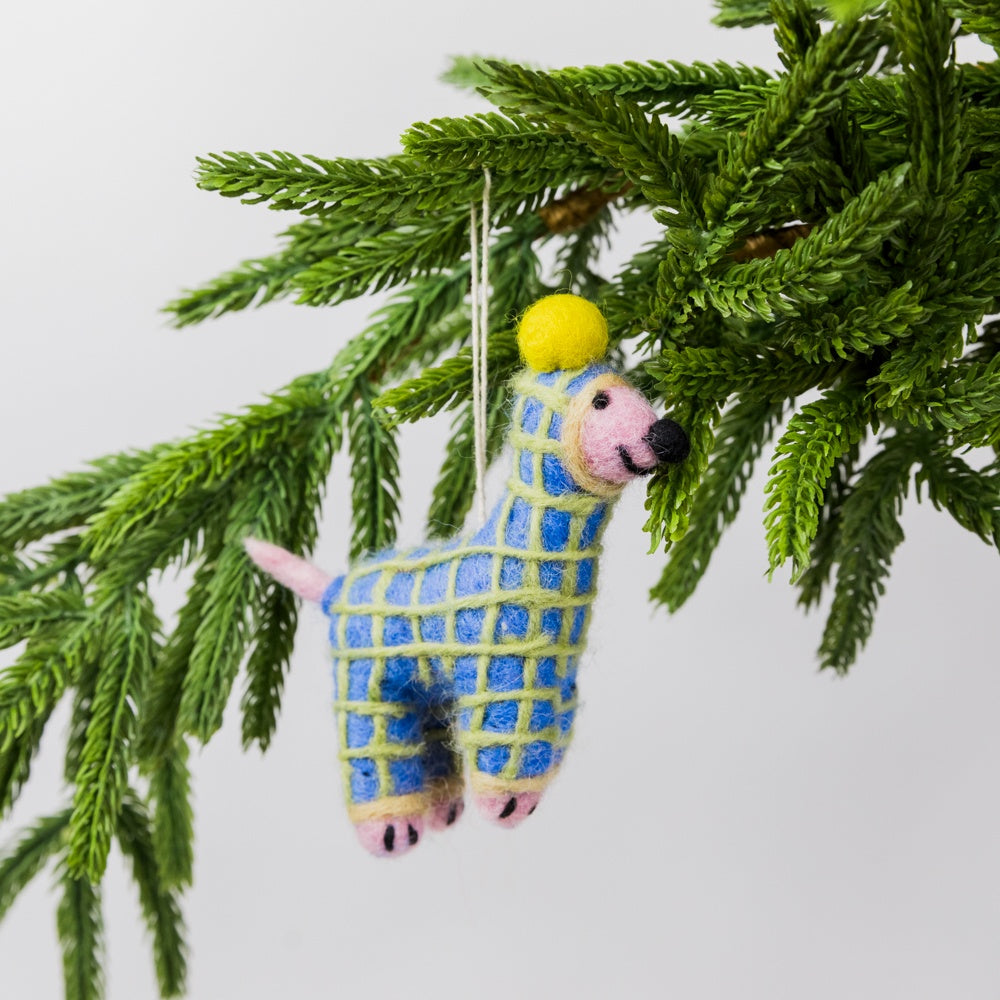 Decorative dog in a onesie ornament in blue and yellow pattern hanging on a green branch.