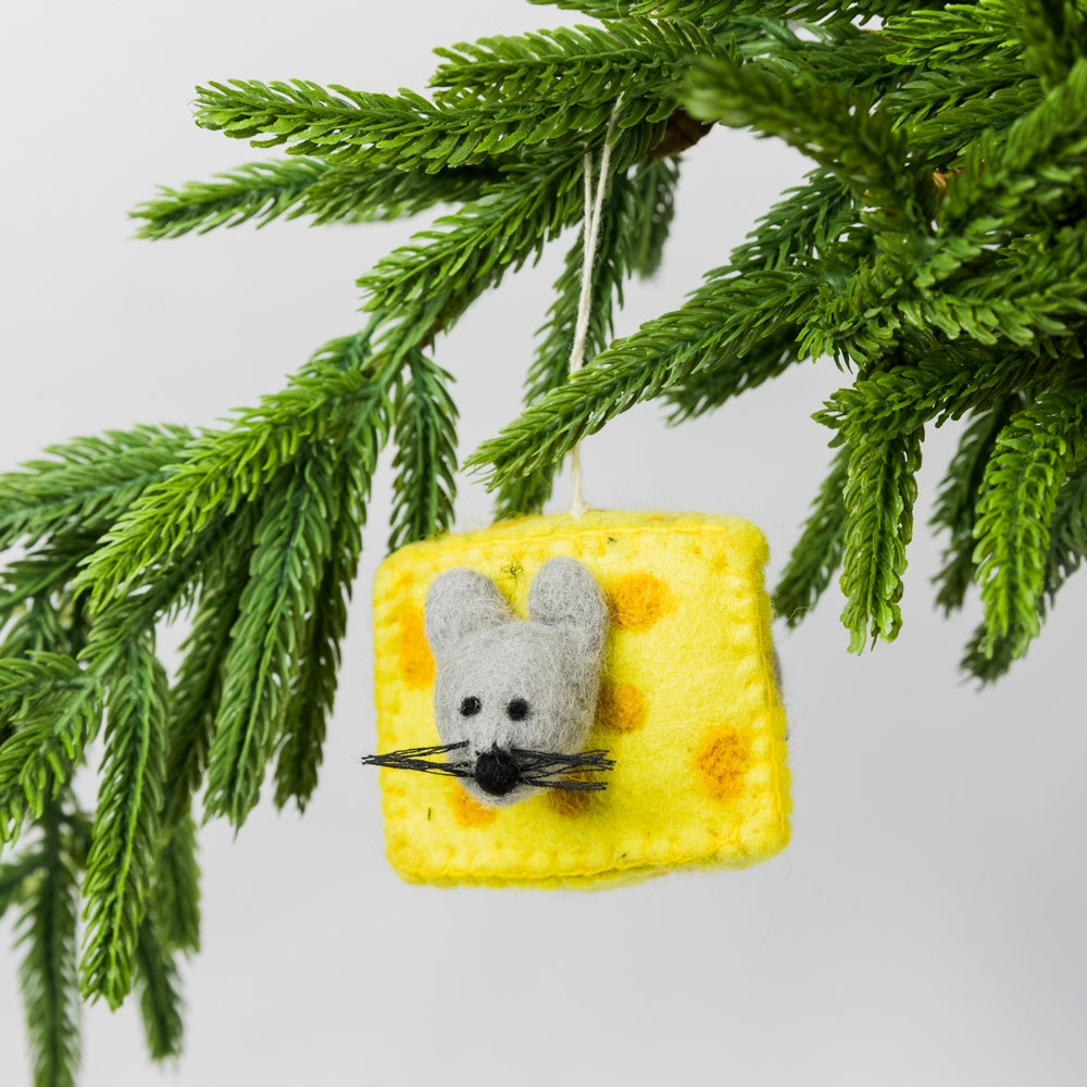 Decorative ornament shaped like a wedge of cheese with a mouse figure hanging from a Christmas tree branch