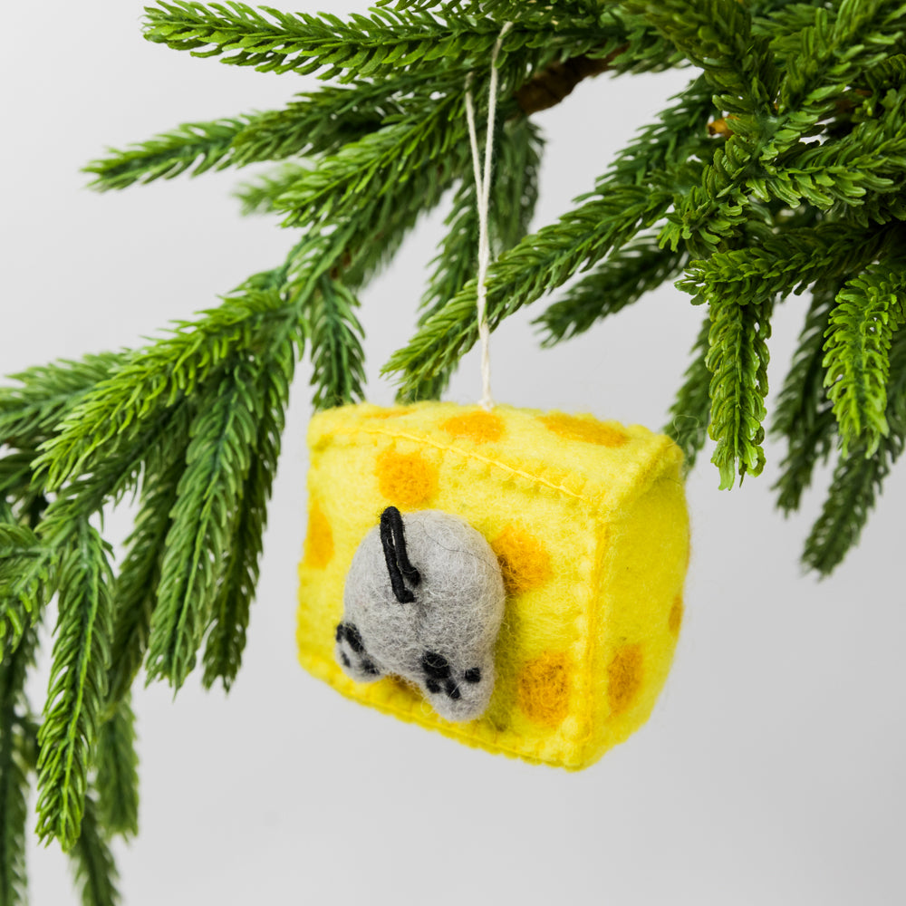 Decorative ornament shaped like a wedge of cheese with a mouse figure hanging from a Christmas tree branch